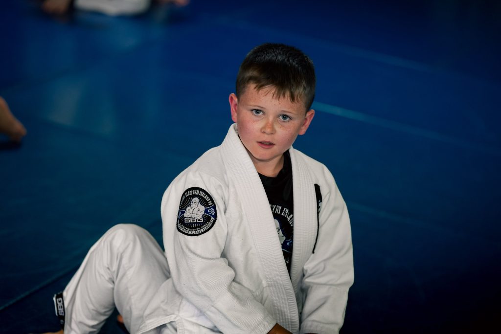 Boy in a white SBG gi sitting on the blue mats
