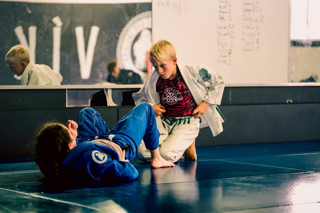 Boy in a white gi training Brazilian Jiu-Jitsu with a partner on the mats